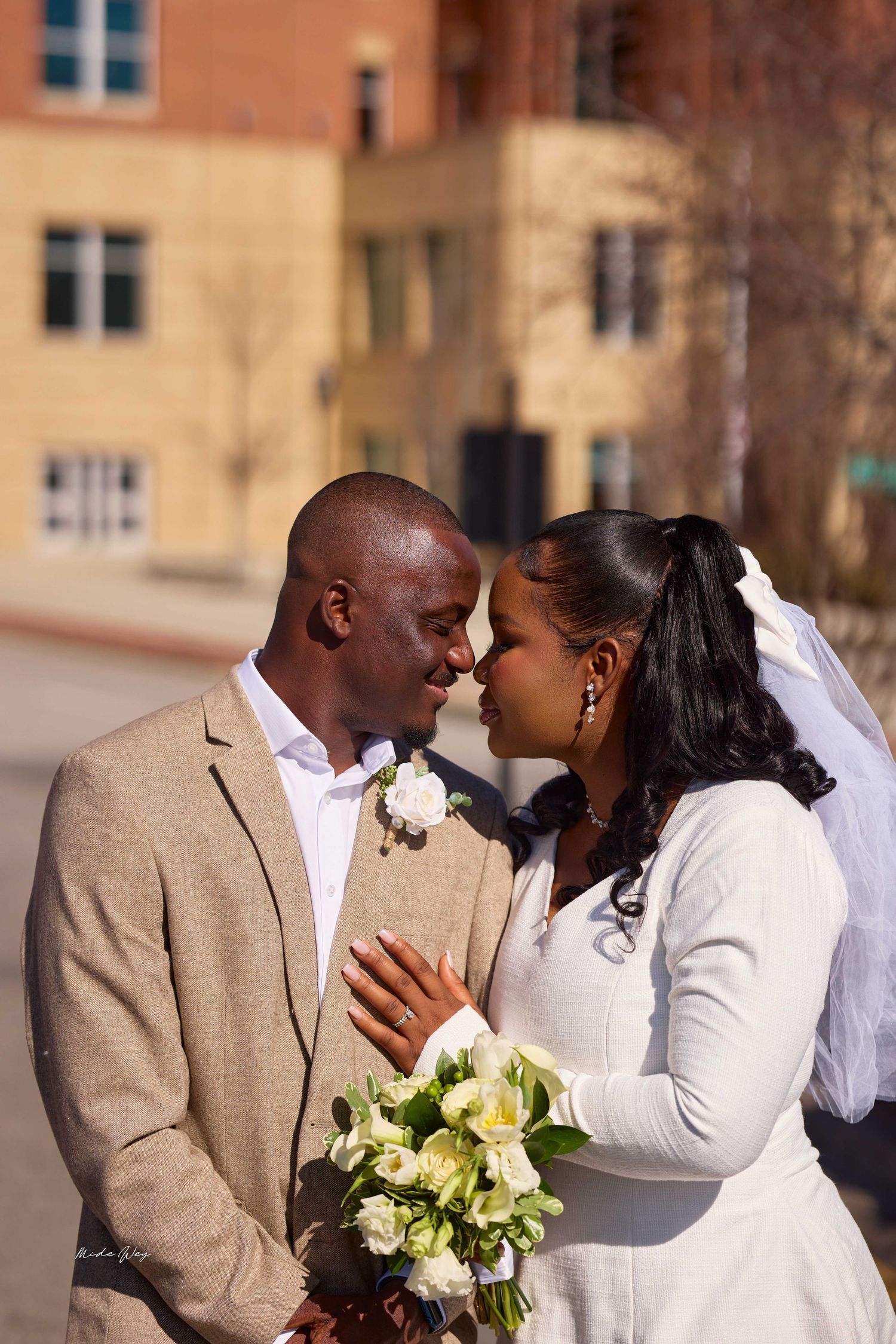 A Black bride and groom share an intimate moment, touching foreheads, as she holds a white bouquet.