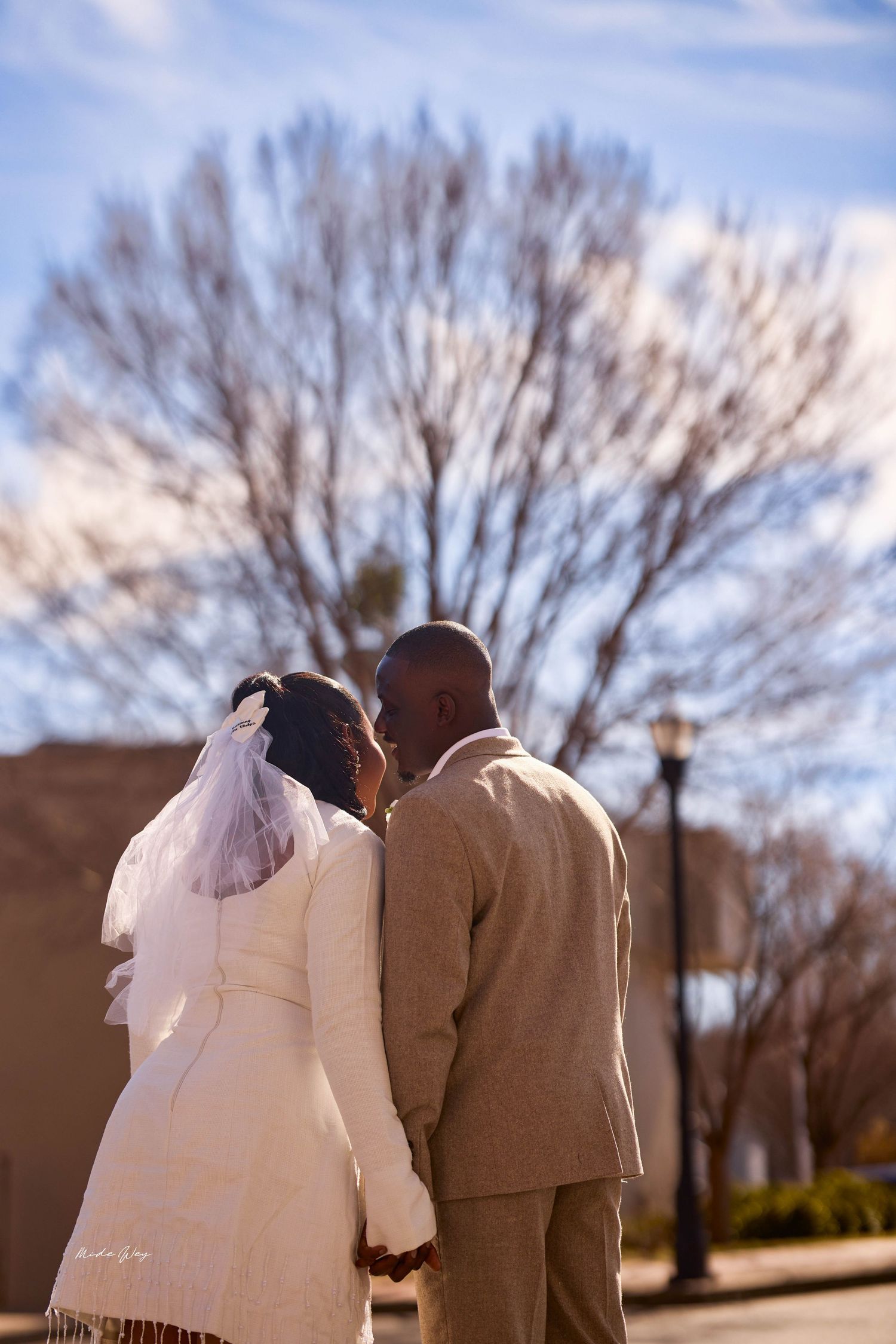A Black bride and groom share an intimate moment outdoors, with the bride in a white dress and veil on their wedding day.