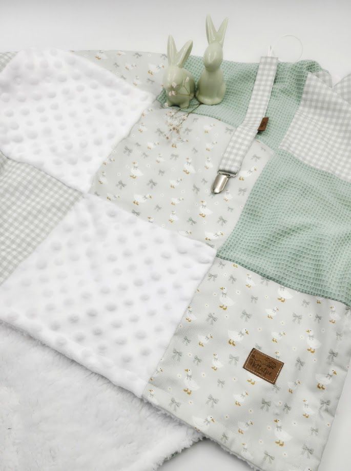 Baby giraffe-print blankets, burp cloths, and muslin swaddles arranged in a wicker basket with tan booties.