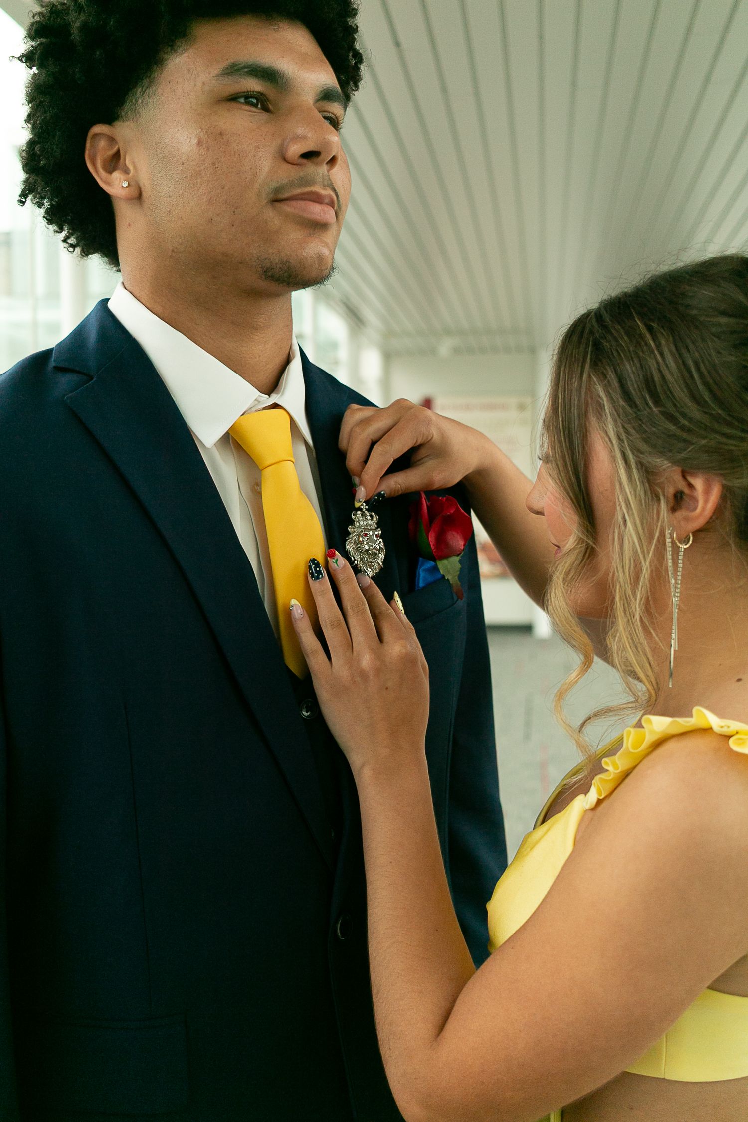 A young woman in a yellow dress pins a boutonniere on her prom date's navy suit with a yellow tie.