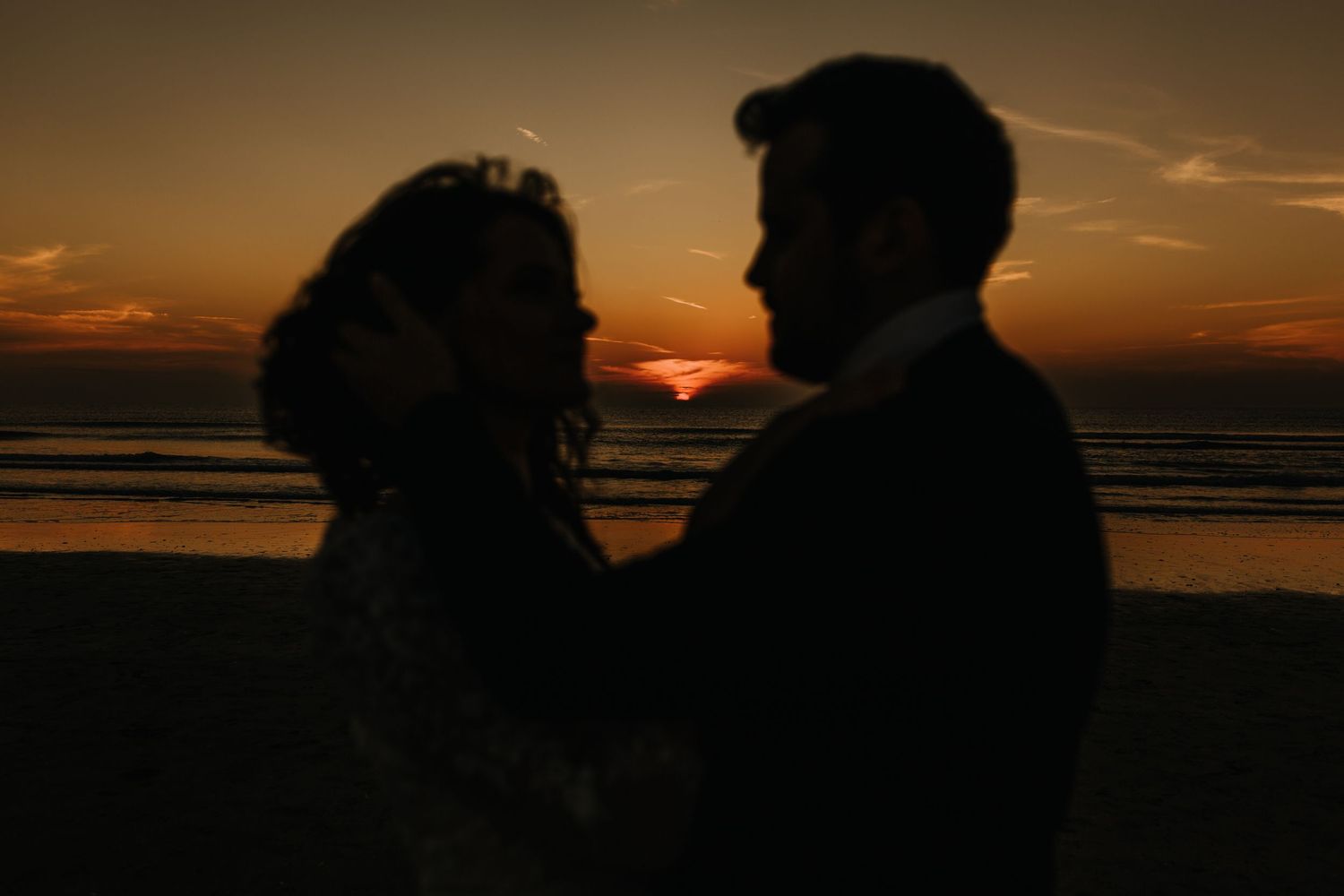 Romantic bride and groom embracing at golden sunset hour in a dreamy backlit outdoor setting.