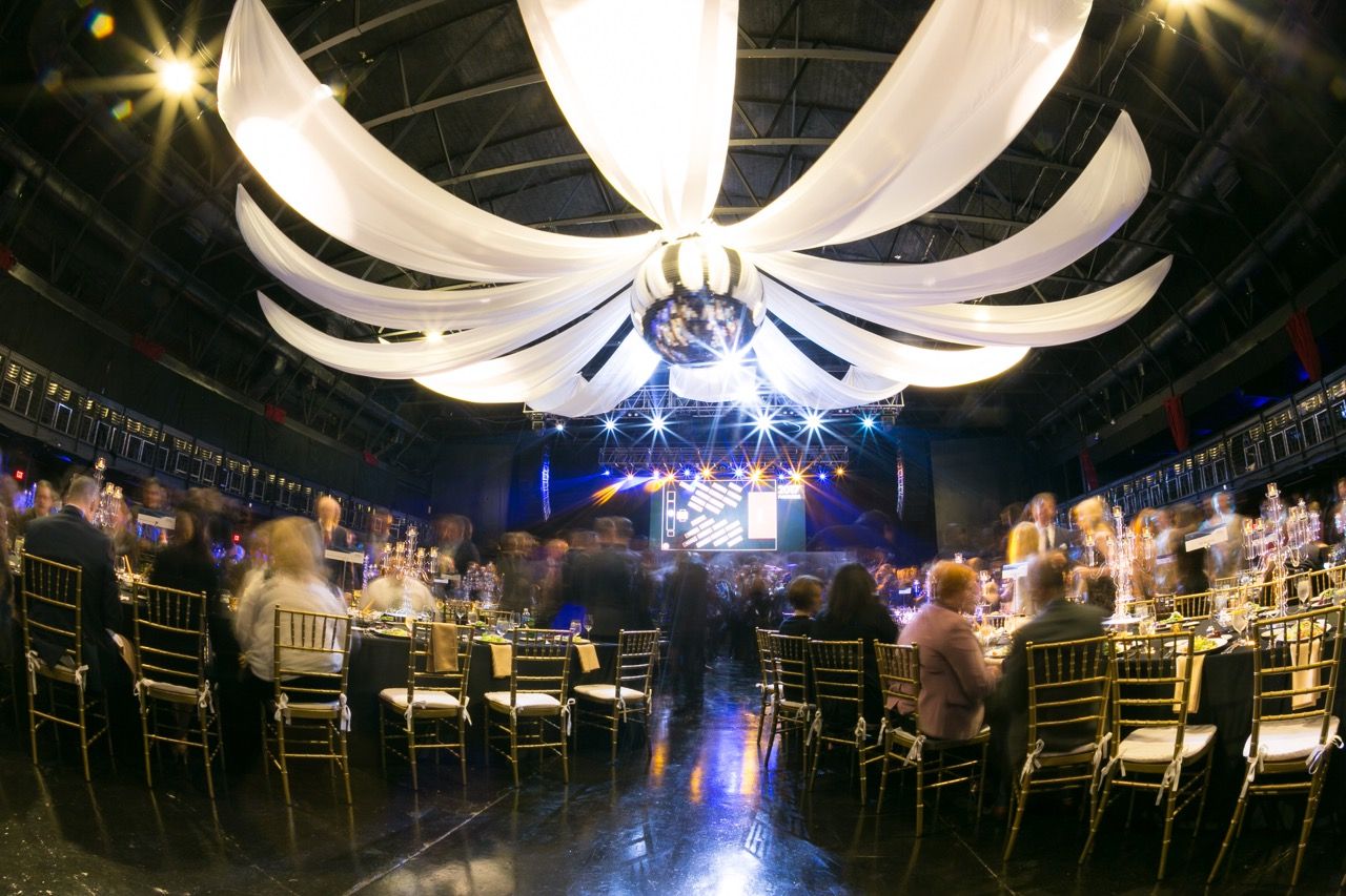 Elegant banquet hall with draped white ceiling, gold chairs, and stage lighting at a formal gala event.