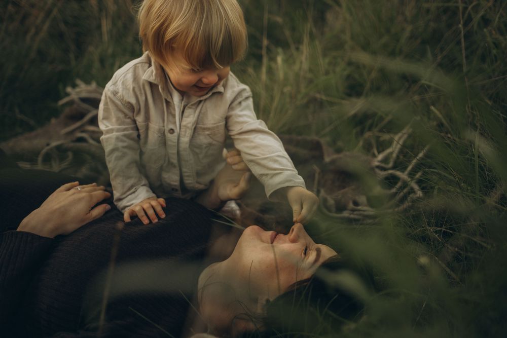little boy tickling her mom's nose with grass during outdoor family photoshoot in Stockholm while being captured by family photographer