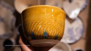Close-up of amber glazed ceramic cup with blue drip accents and textured surface in pottery studio.