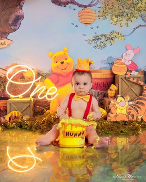 Baby smashes Hunny cake at Winnie the Pooh first birthday party with neon sign.