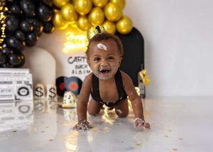 A baby boy crawls with cake on his face at a Carter black and gold hip-hop themed first birthday cake smash.