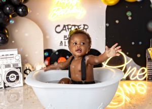 A baby boy sits in a white tub surrounded by bubbles at a Carter hip-hop music themed first birthday party.