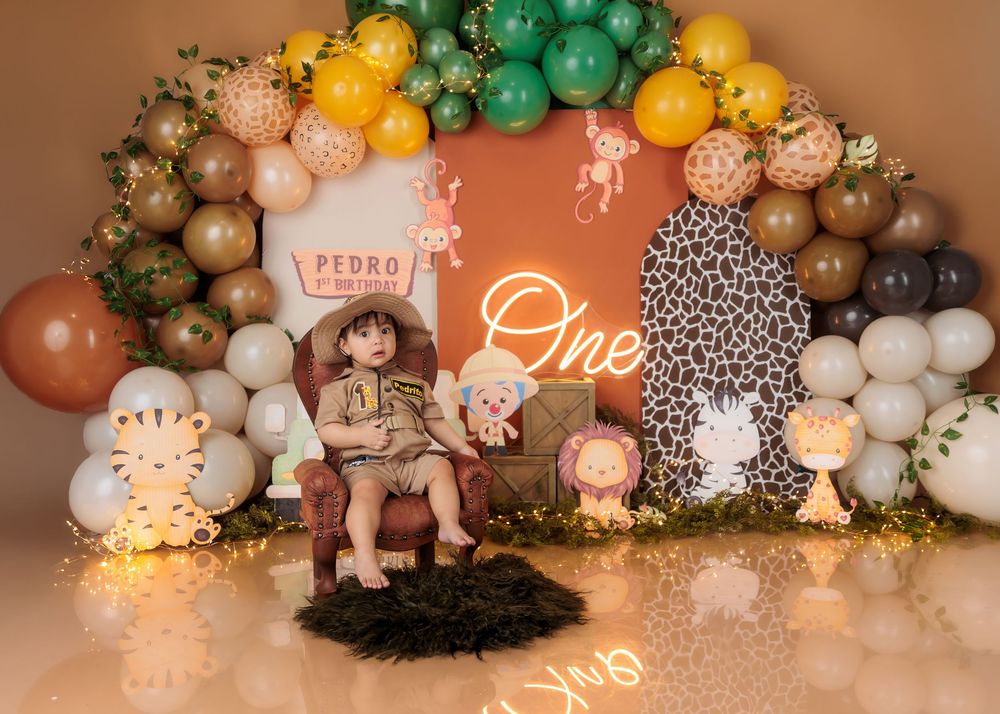 Young child in safari costume sits in chair at Pedro's wild animal-themed first birthday party setup.