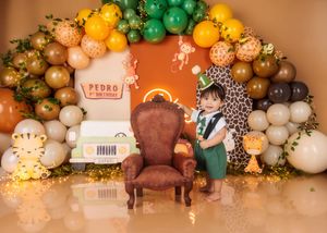Toddler in green outfit stands beside a large chair at Pedro's safari-themed first birthday celebration.