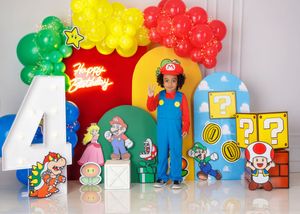 Child in Luigi costume stands beside Super Mario themed balloon arch and character cutouts for 4th birthday.