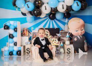 Baby in tuxedo sits among Boss Baby themed blue, black, and white balloon garland and dollar sign props.