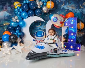 Child in astronaut suit rides inflatable shuttle under blue space-themed balloon arch with number 1.