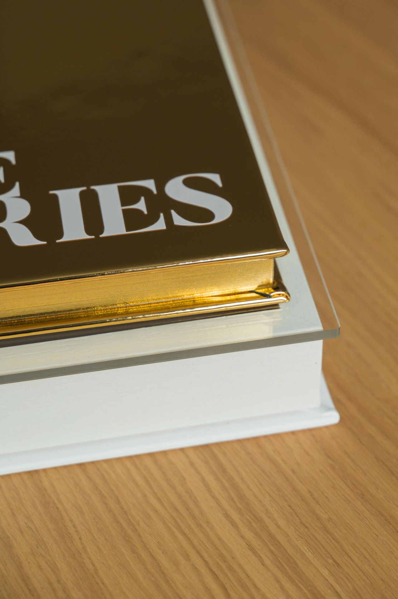 Corner detail of gold metallic Love Stories photo book resting in white acrylic display case.