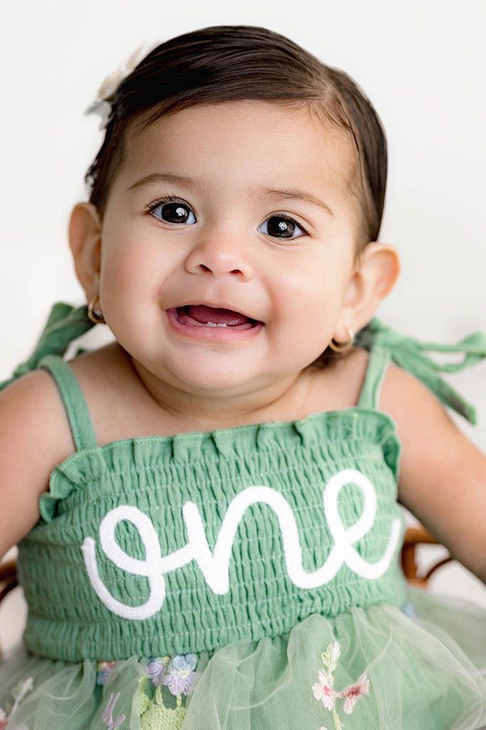 Adorable baby girl in green smocked one dress smiling for first birthday portrait photo session by Menifee baby photographer.