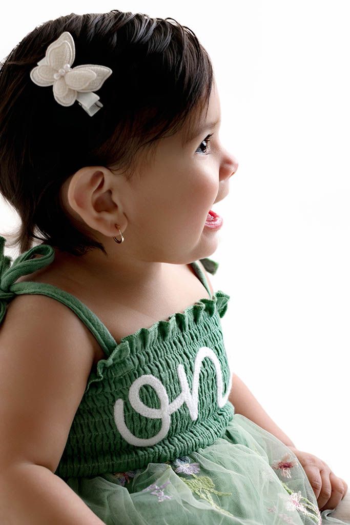 A baby girl in a green smocked dress with “One” embroidery and butterfly hair clip celebrates her first birthday.