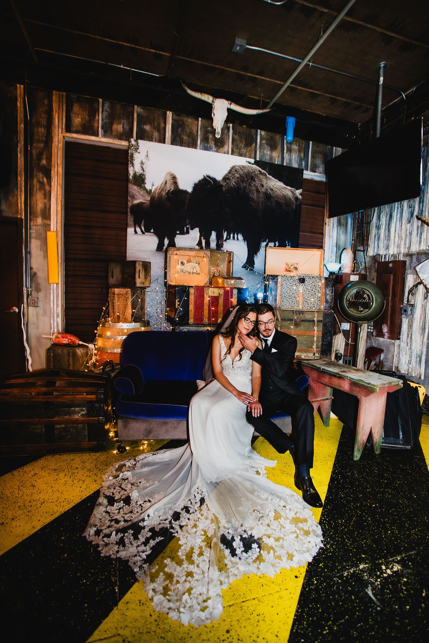 Wedding couple poses in artistic venue with large buffalo artwork and flowing lace dress.