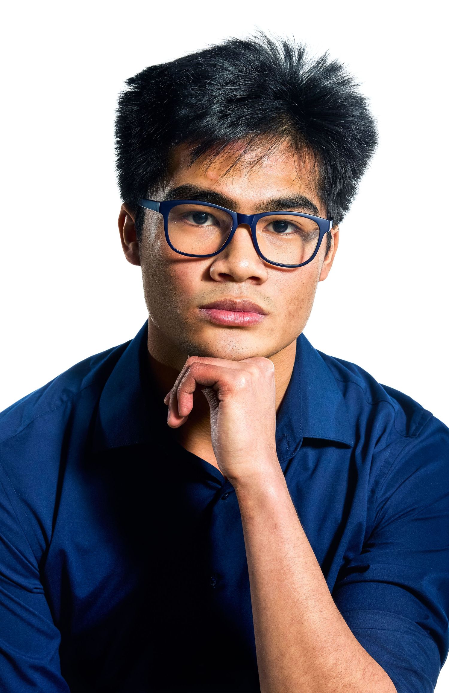 Close-up studio portrait of a man with blue glasses resting his chin on his hand.