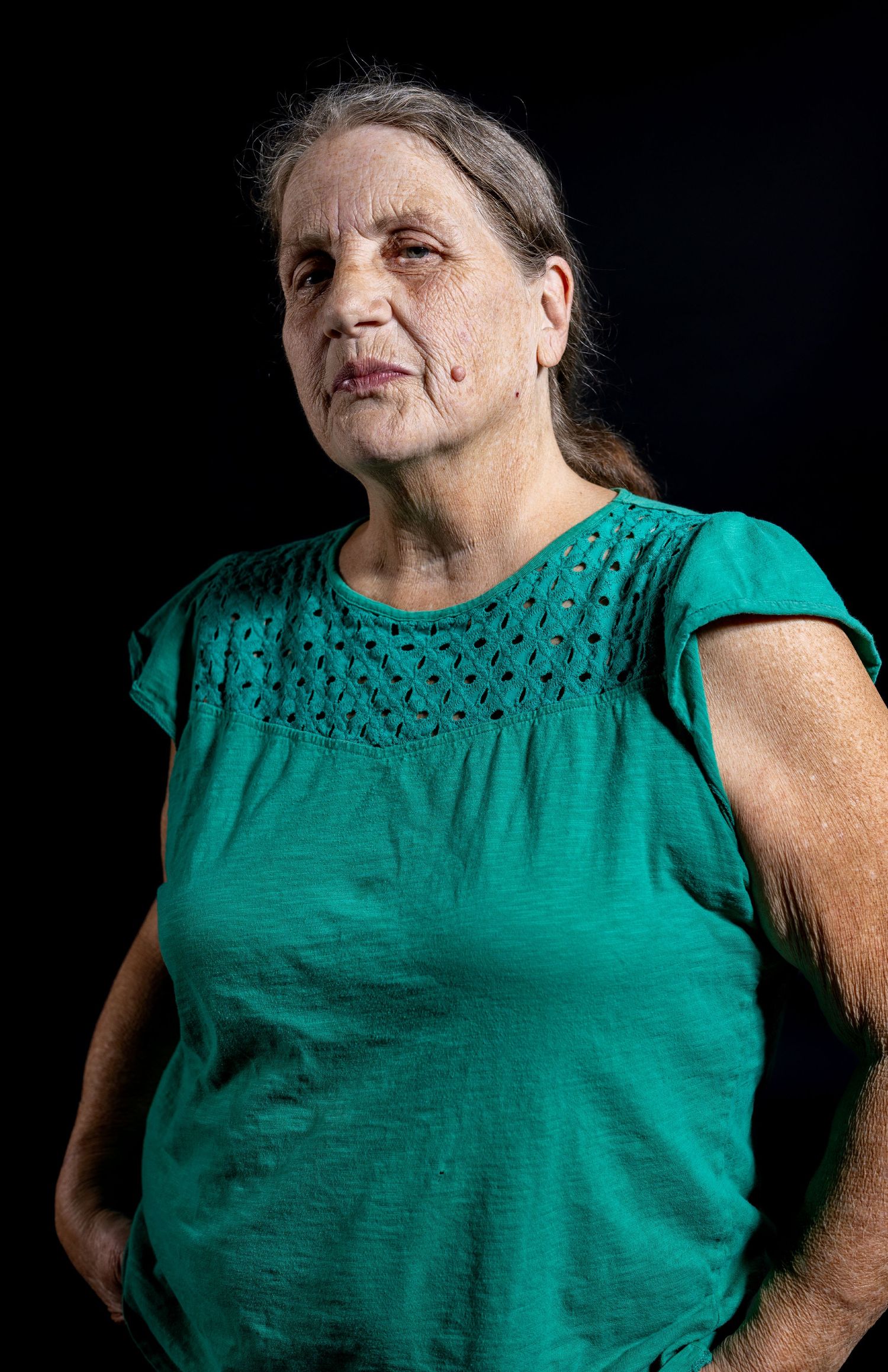 Studio portrait of a woman in a teal shirt against a black background.