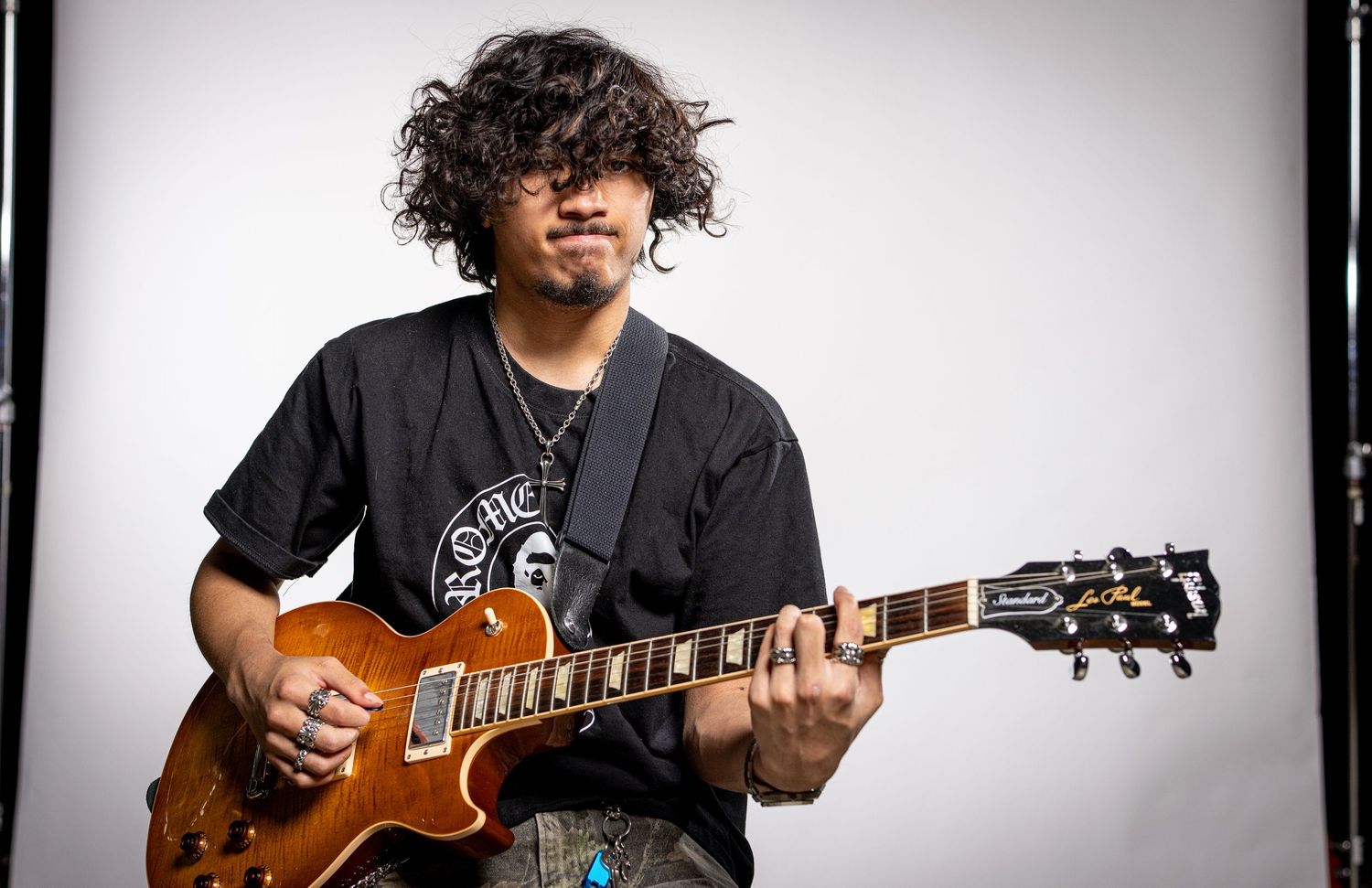Musician plays an electric guitar in a studio portrait against a light background.