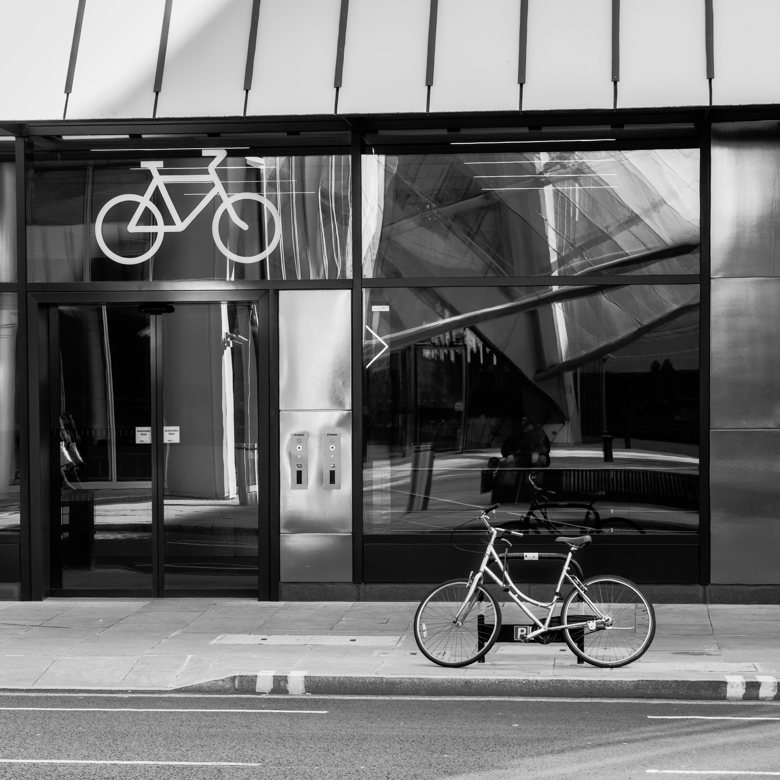 Black and white photo of a bicycle parked outside a glass building facade