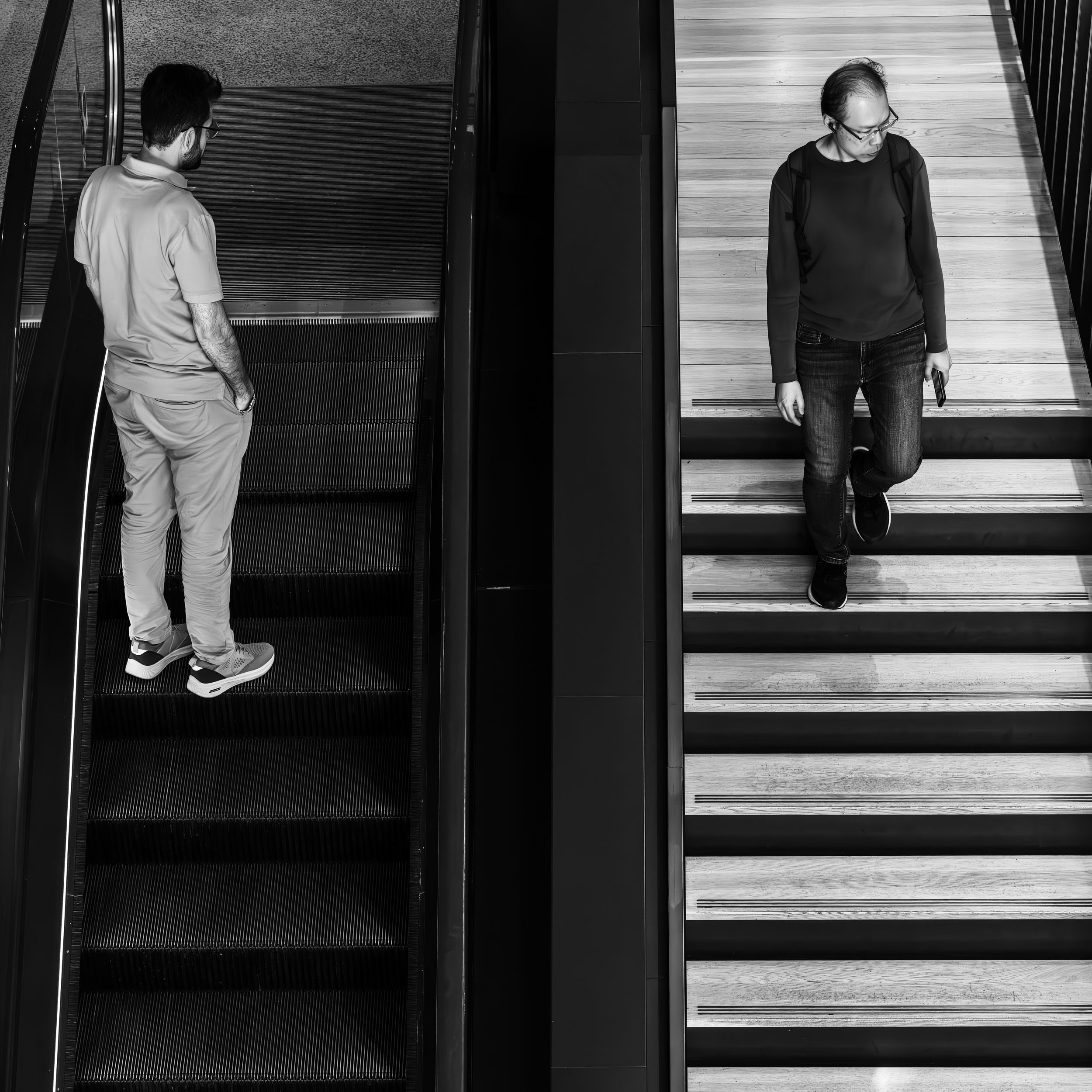 Symmetrical black and white street photo of two men walking on parallel staircases