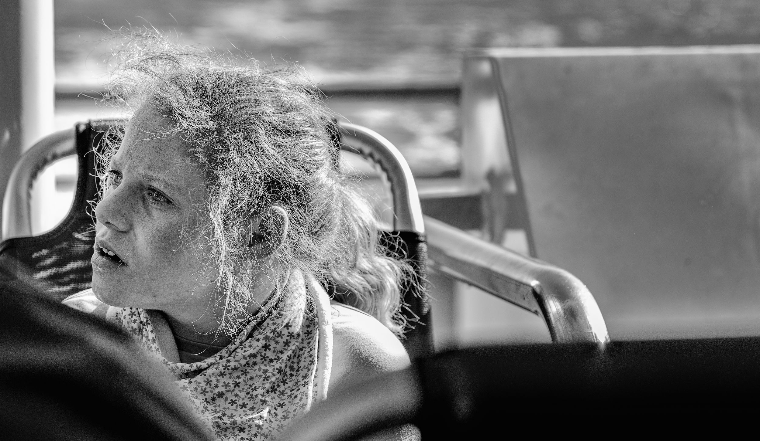 Black and white candid portrait of an elderly woman looking out from a bus seat