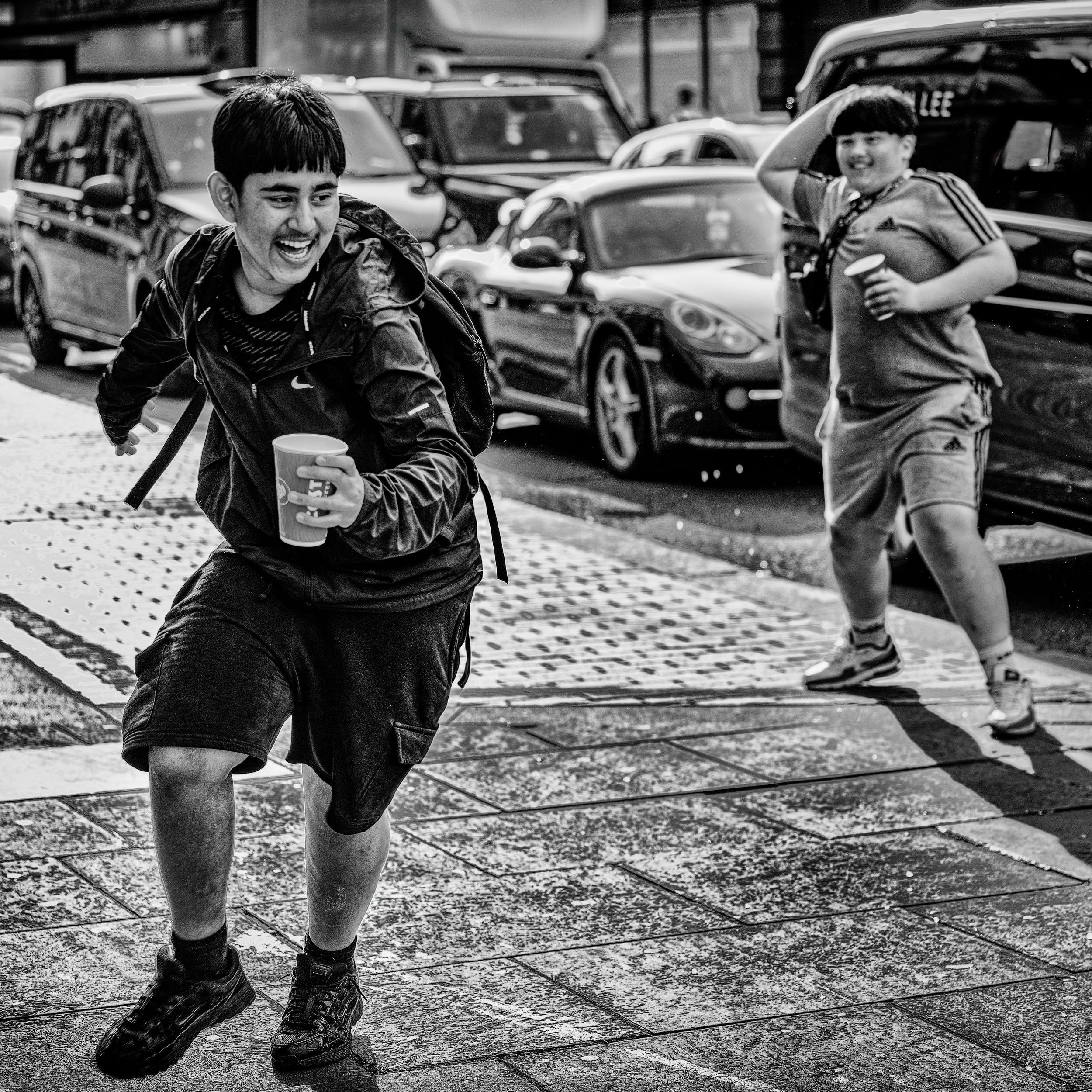 Black and white candid street photography of a boy running across a street with cars
