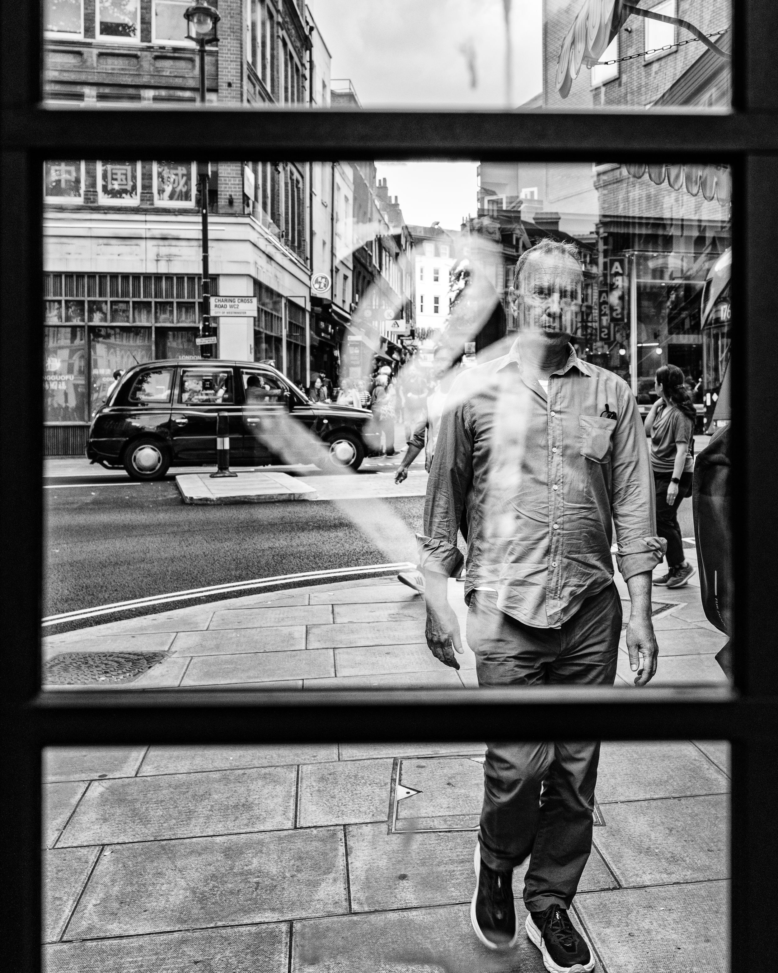 Black and white street photography of a man seen through a shop window on an urban street
