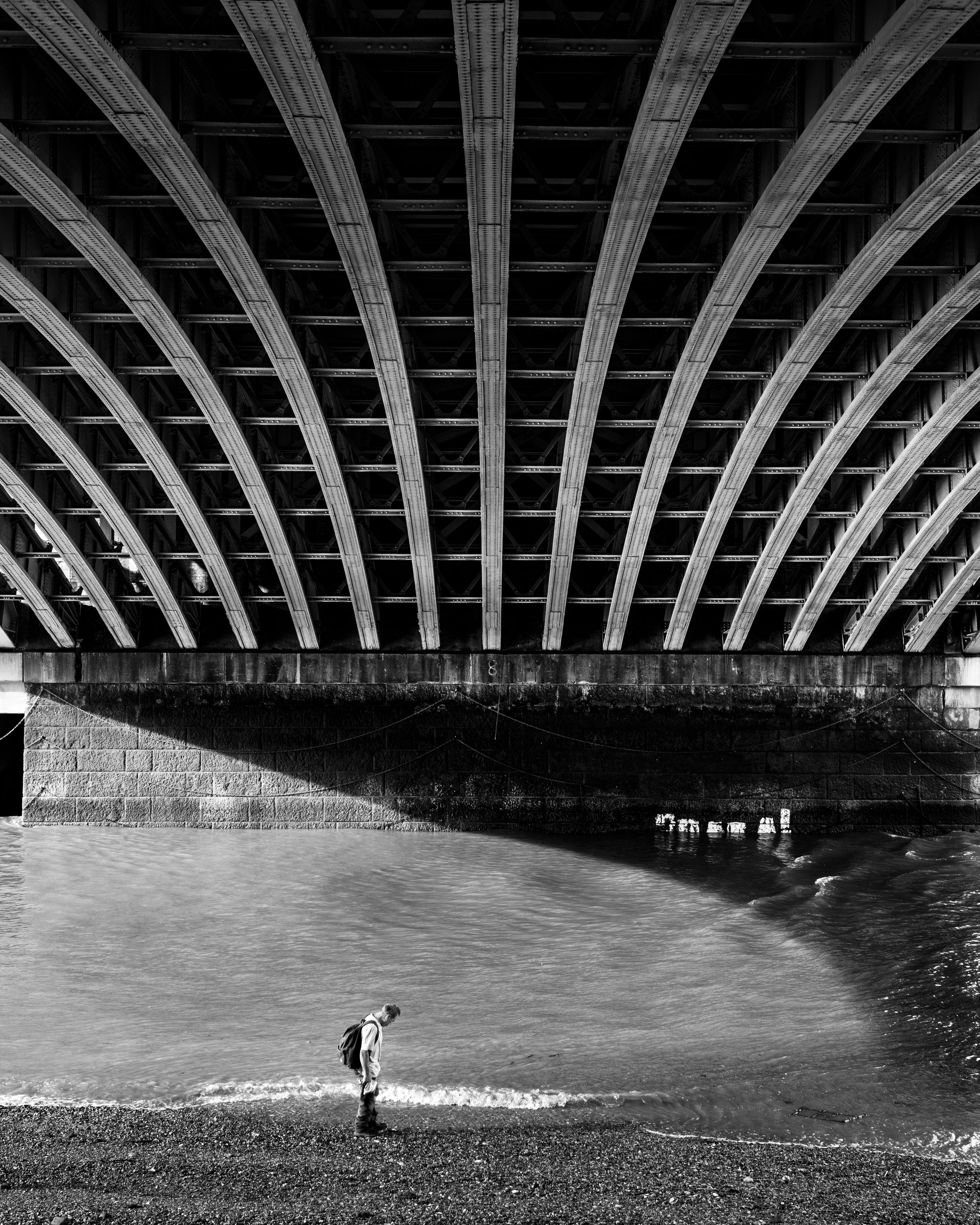 Minimalist black and white photo of a person beneath an arched bridge structure