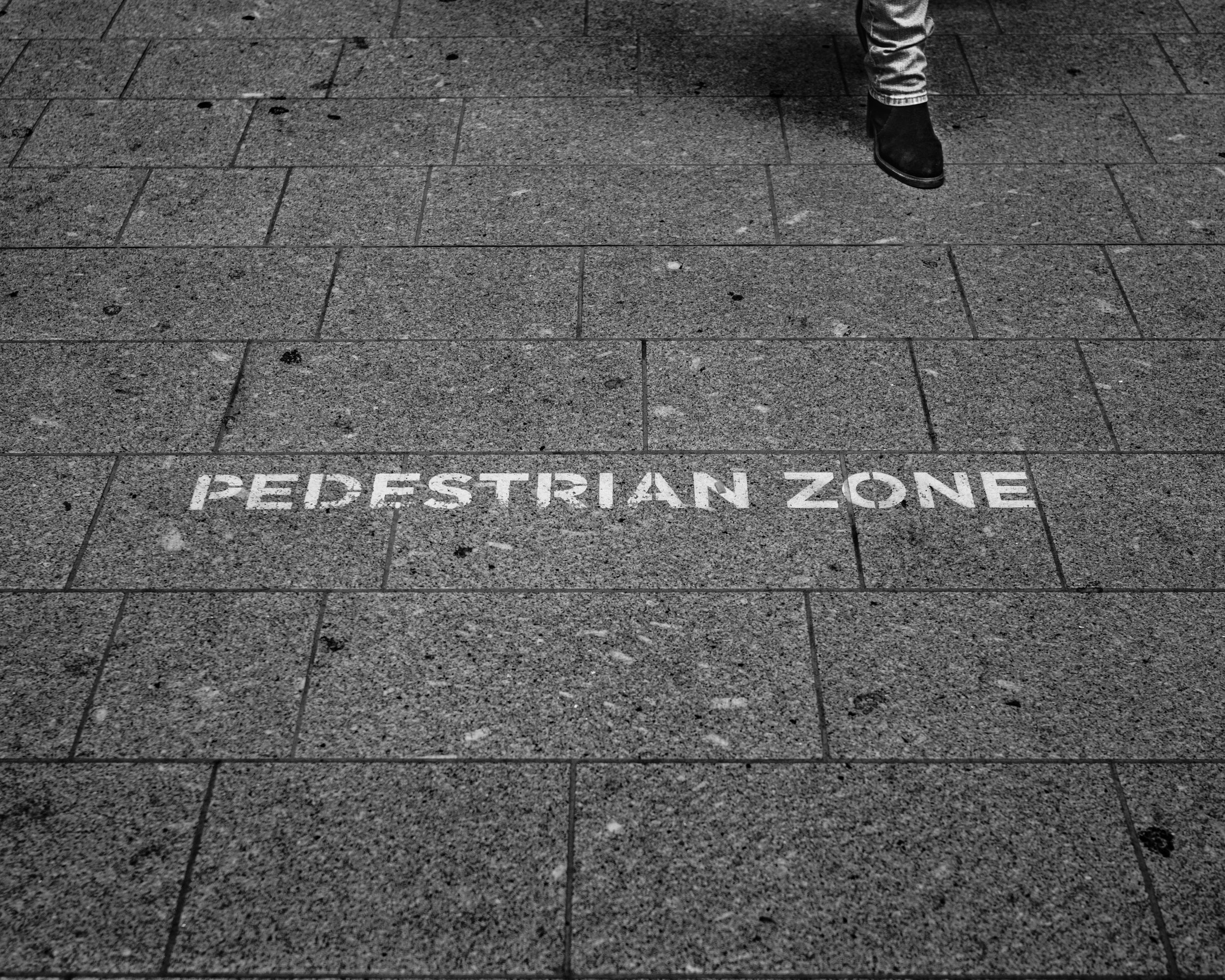 Black and white street photography of a pedestrian zone sign painted on the pavement