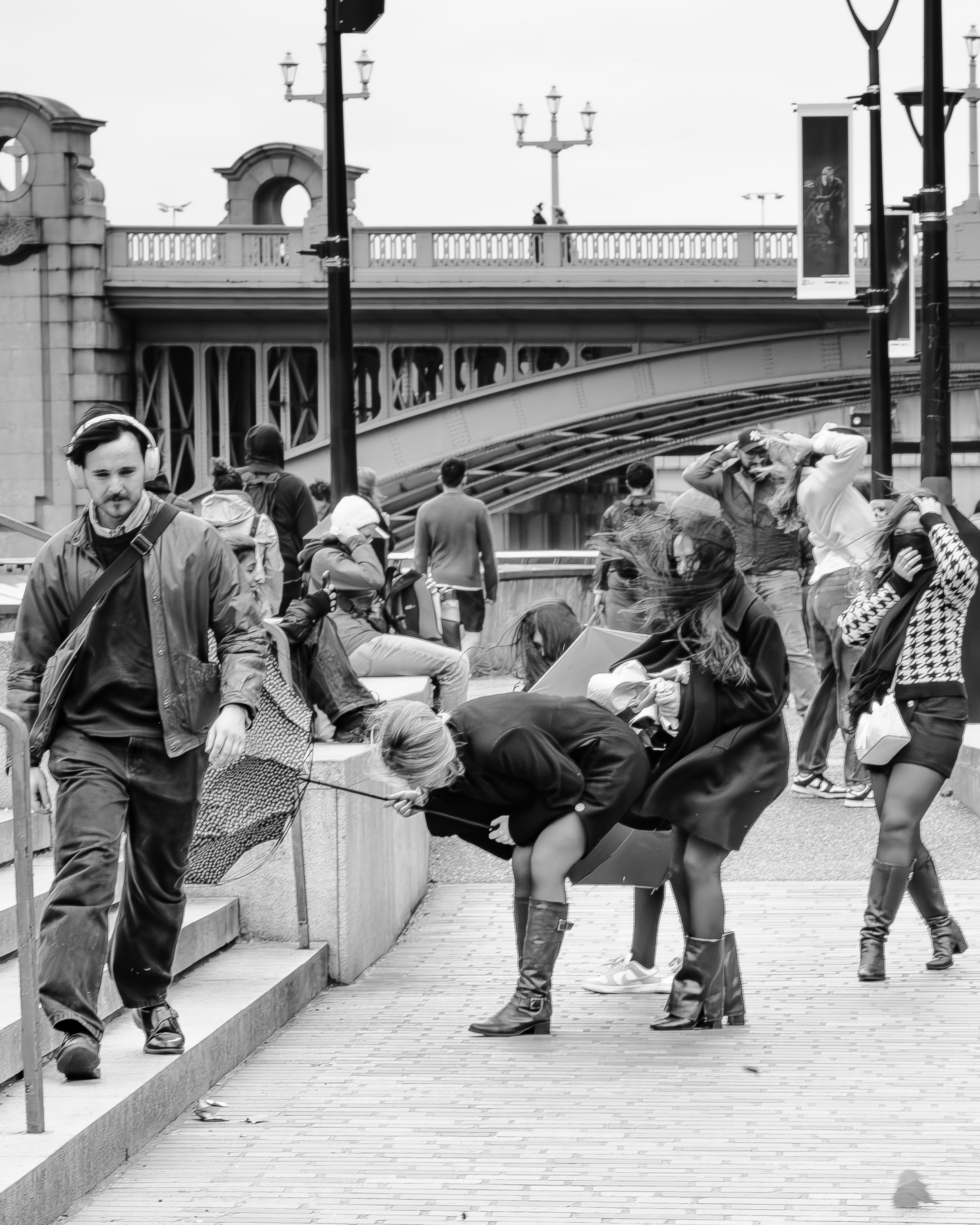Black and white street photography of people walking a dog beneath a railway bridge