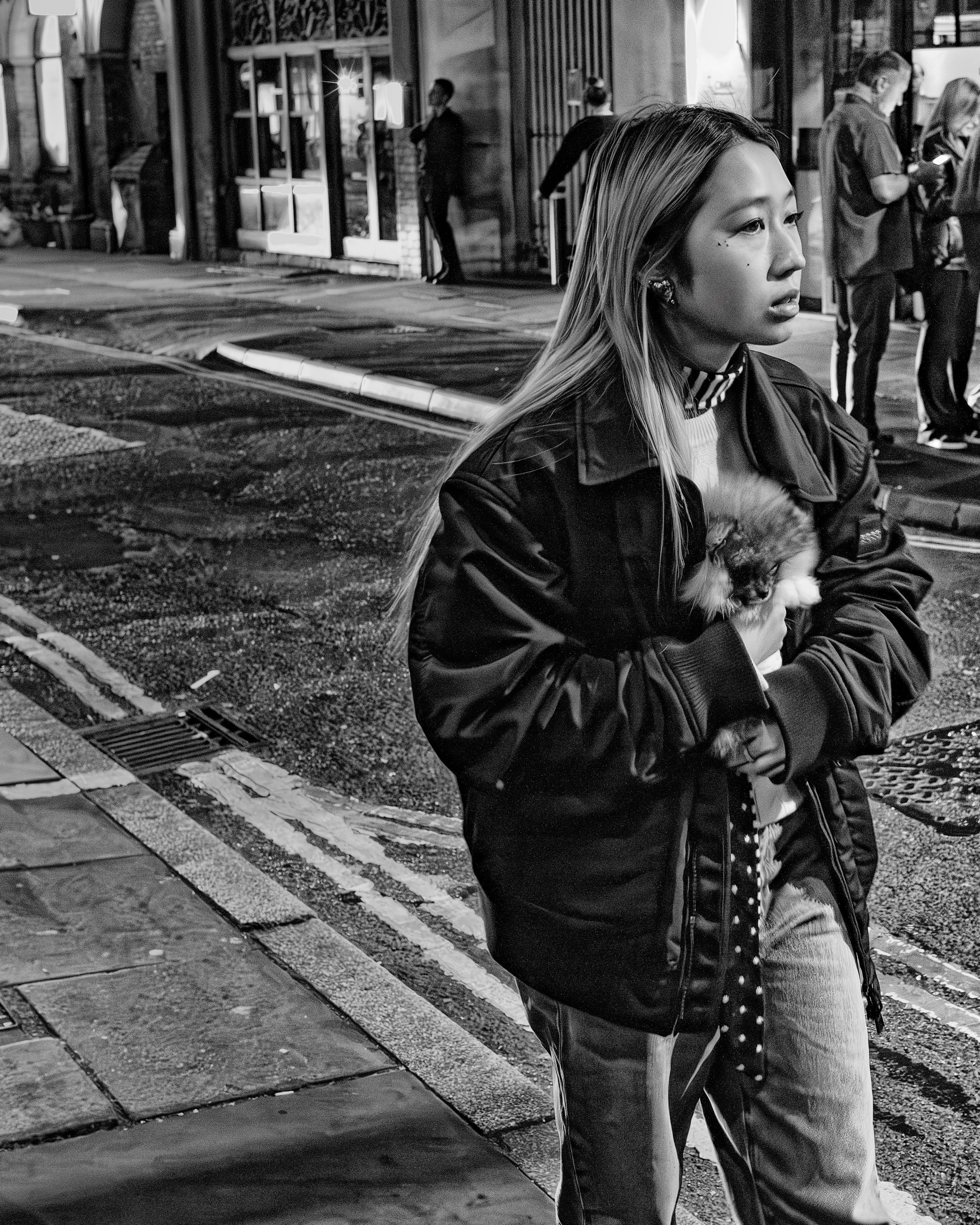 Black and white candid street portrait of a young woman standing on a city corner