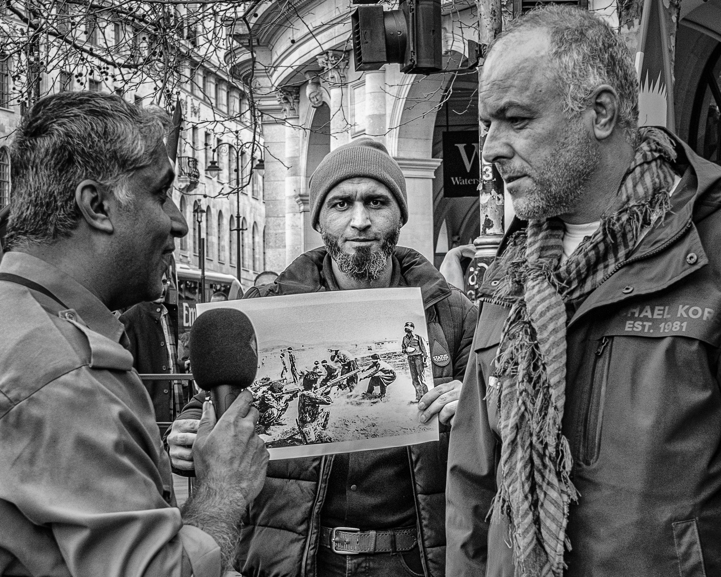 Black and white street photography of a man being interviewed with a microphone in a crowd