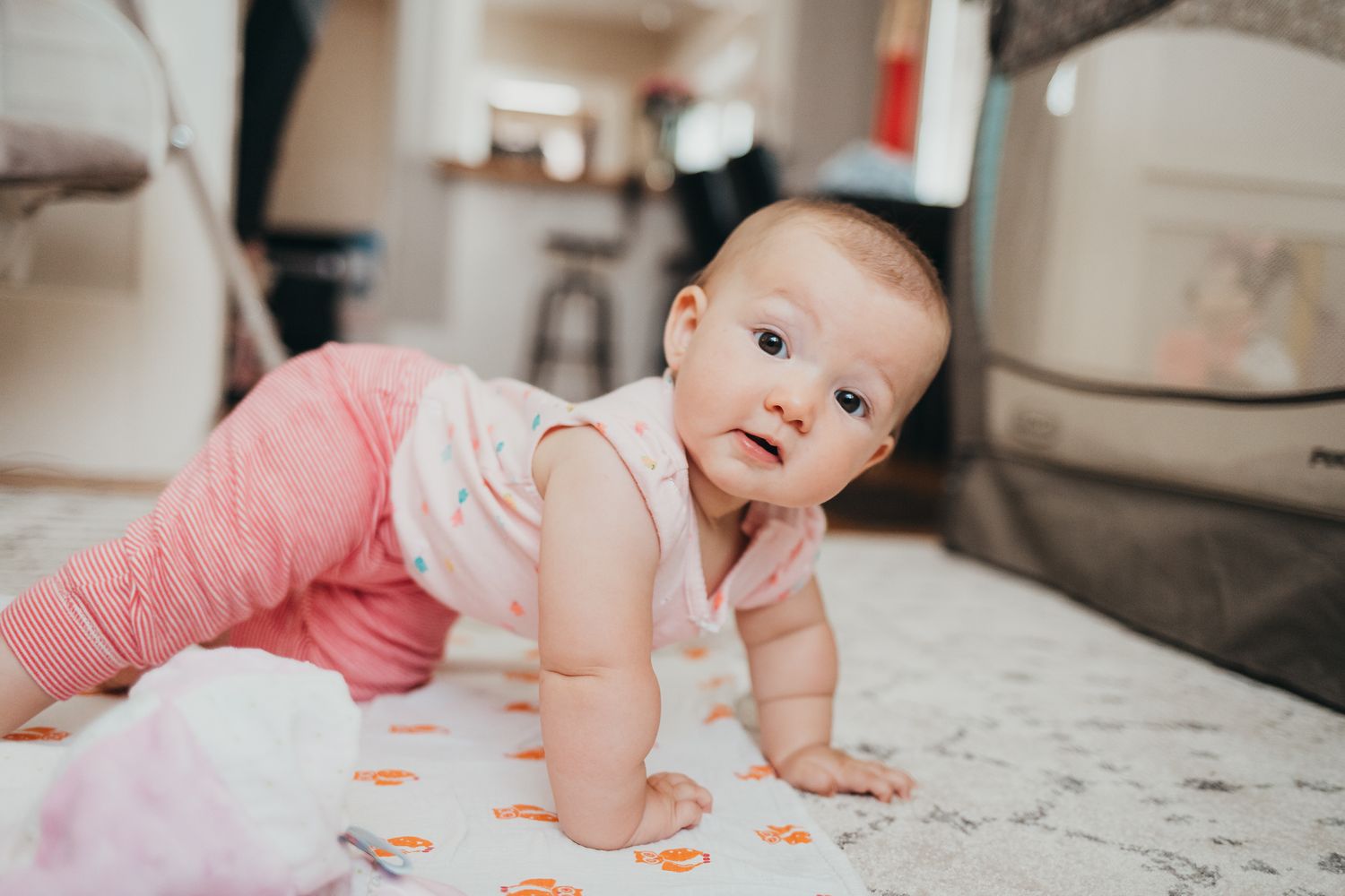 Adorable smiling baby with bright eyes doing tummy time on a soft white blanket in a cozy home setting.