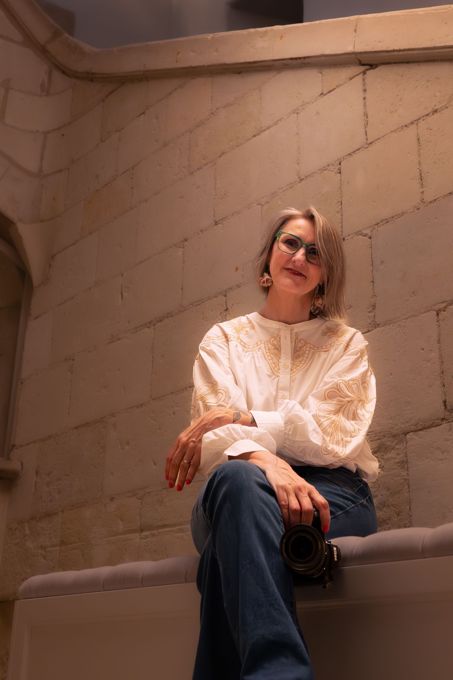 La photographe Stéphanie Lecaudé assise détendue sur le rebord d'un mur en pierre de l'Abbaye de Villeneuve en Loire Atlantique