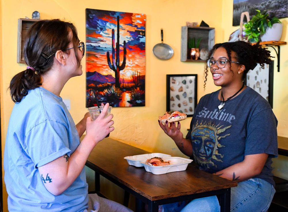Two women enjoying pizza slices together at a casual restaurant with colorful desert artwork on yellow walls.