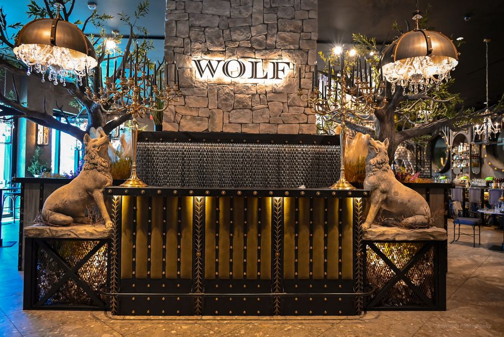 Elegant Wolf restaurant entrance with golden deer statues flanking a studded bar, chandeliers, and illuminated sign.