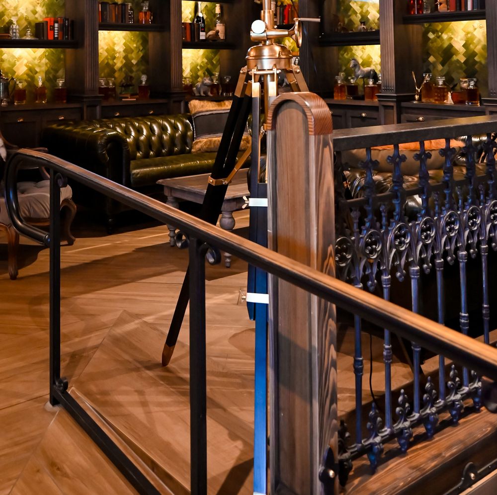 Elegant restaurant interior with ornate black iron railing, wood floors, green leather booths, and warm ambient lighting.