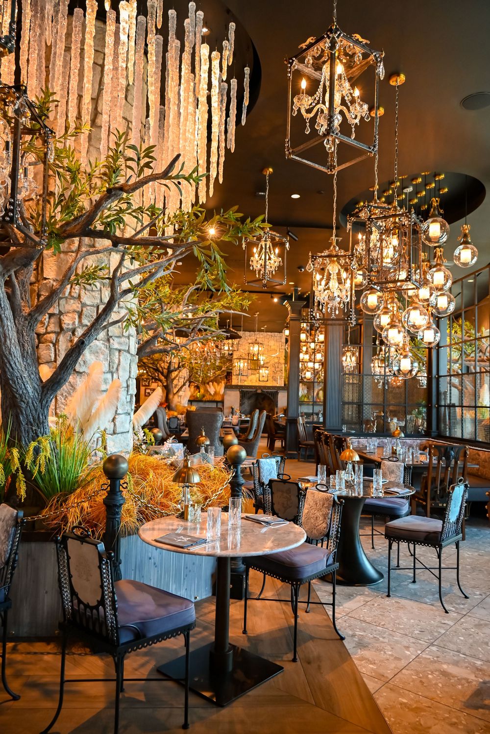Elegant restaurant interior with hanging lanterns, lush trees, and intimate dining tables in a warmly lit ambiance.