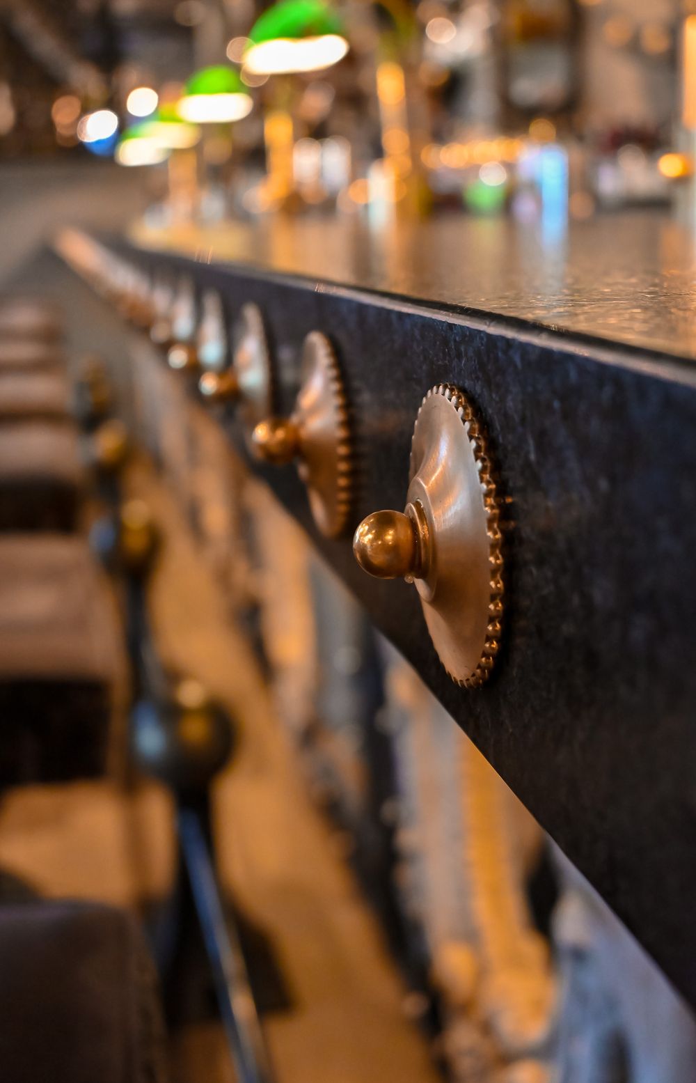 Close-up of ornate brass knobs on a dark bar rail in a warmly lit restaurant interior.