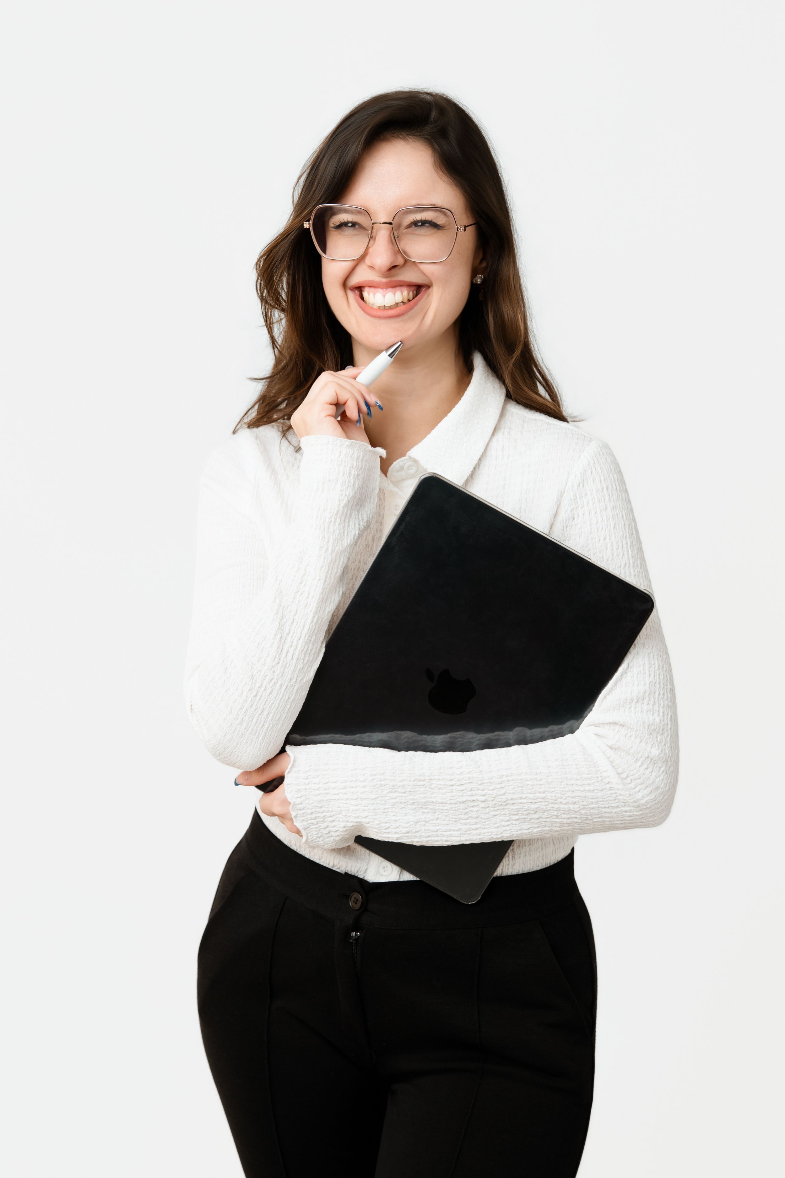 Smiling woman in white sweater and glasses holding laptop and pen against white background.