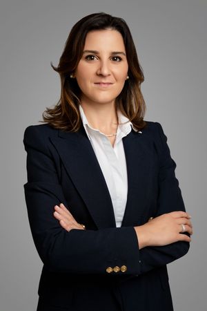 Confident businesswoman in navy suit with arms crossed, smiling against gray studio background.