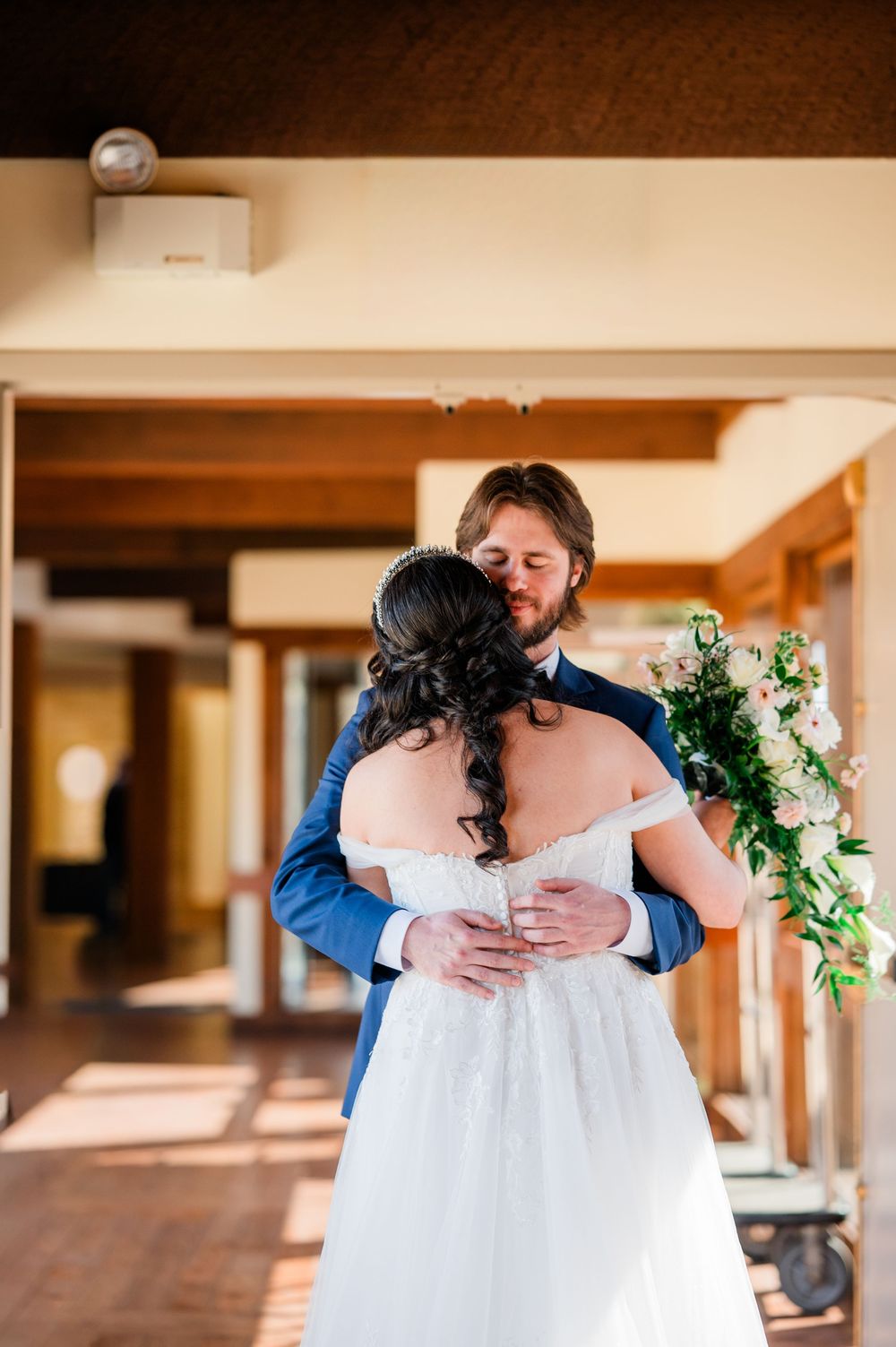 Groom tenderly embraces bride from behind during an emotional first look moment at their wedding venue.