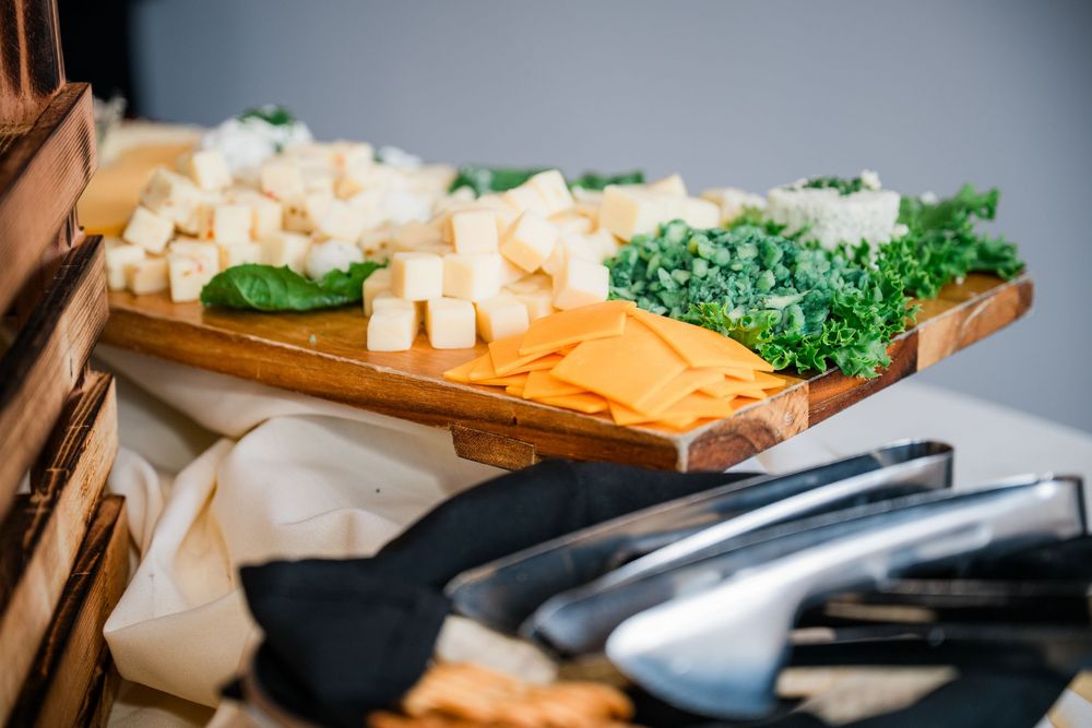 Elegant wedding charcuterie board featuring cubed white cheese, sliced cheddar, and fresh herbs on a wooden cutting board.