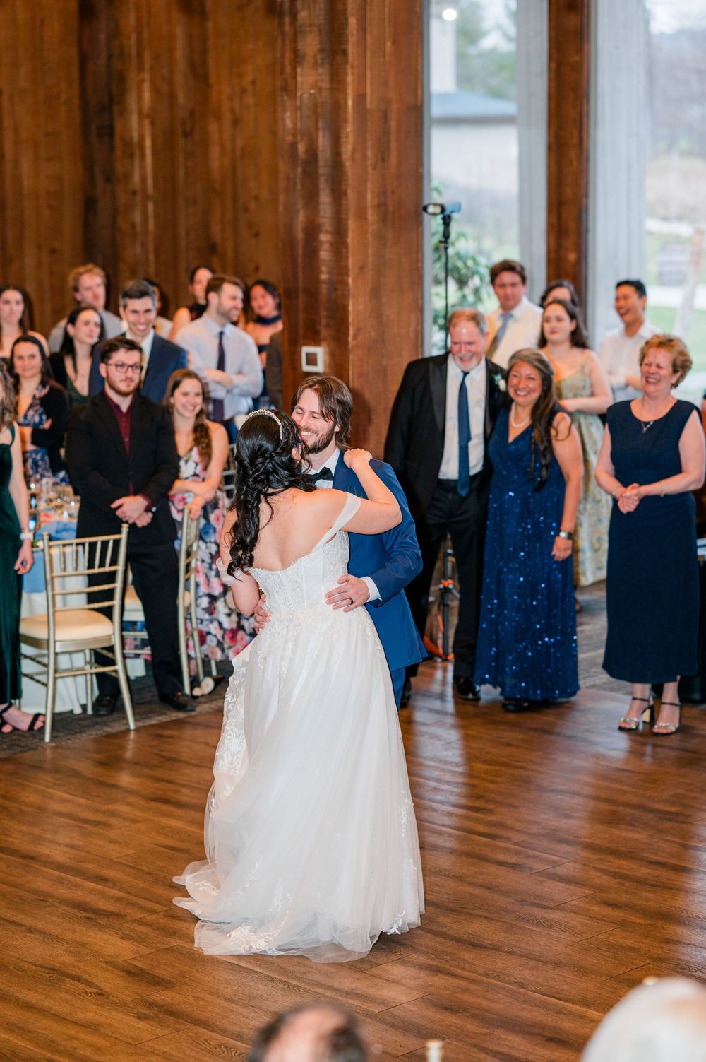 Bride and groom share their first dance as wedding guests watch and celebrate in a rustic barn venue.
