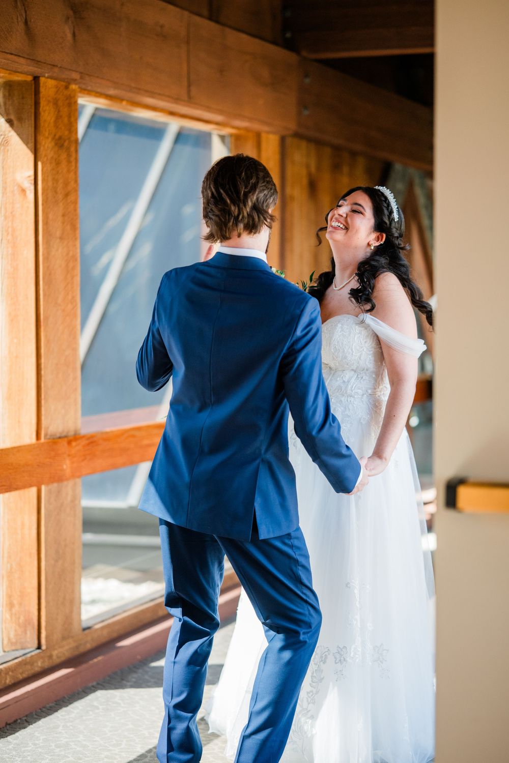 Bride laughs joyfully as groom turns around during a sweet first look reveal at their rustic wedding venue.