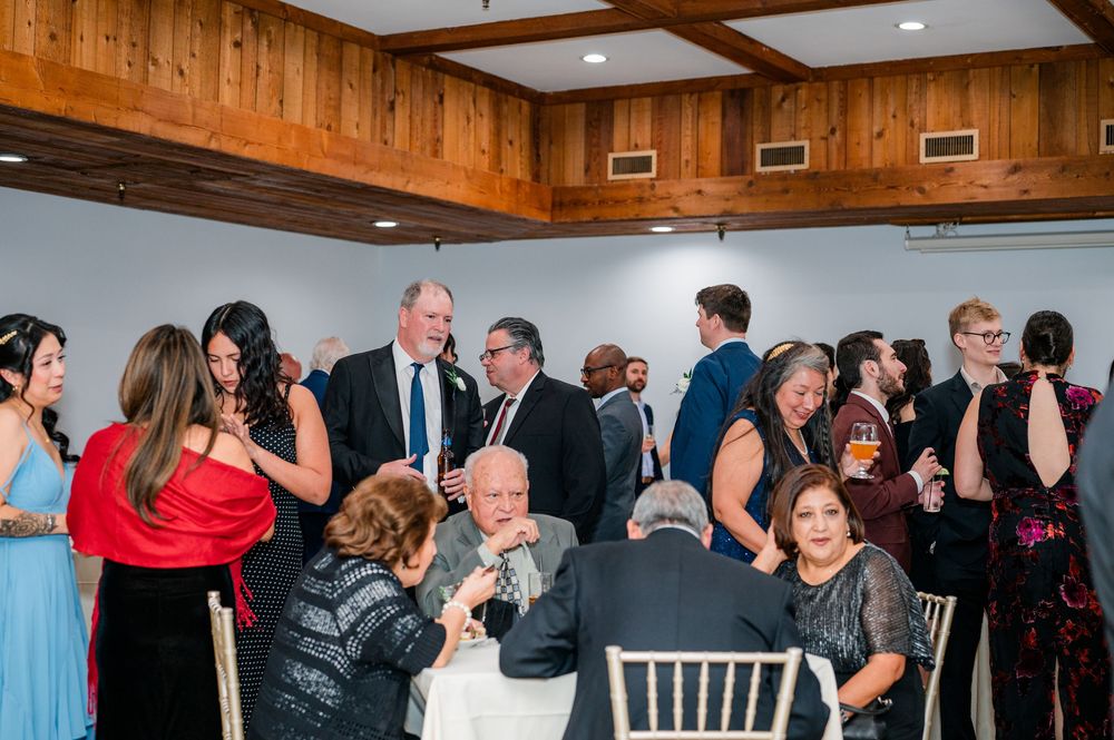 Elegantly dressed wedding guests mingle and socialize during a reception in a rustic wood-paneled venue.