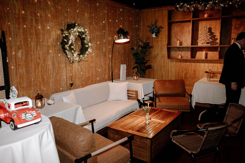 Cozy holiday lounge with white sofas, wood paneling, Christmas wreath, fairy lights, and festive decor for a winter event.
