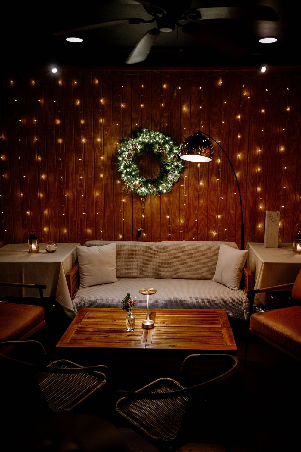 Cozy lounge seating area with fairy lights, green wreath, sofa, and warm ambiance for a wedding reception.