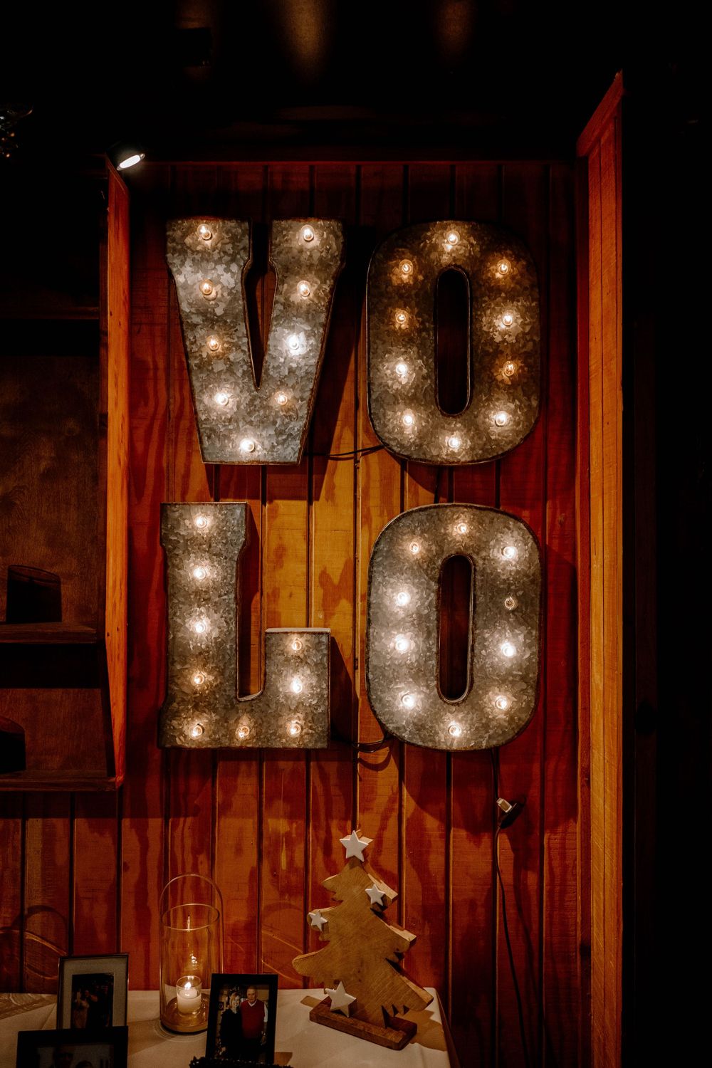 Vintage marquee letters V-O-L-O with Edison bulbs on rustic wood wall with Christmas tree decor.